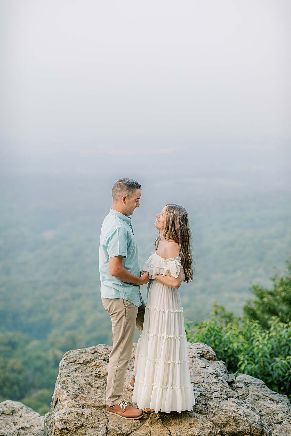 Engagement photo of a couple at Hawk Mountain Sanctuary in PA. The couple stands on rocks with a beautiful view