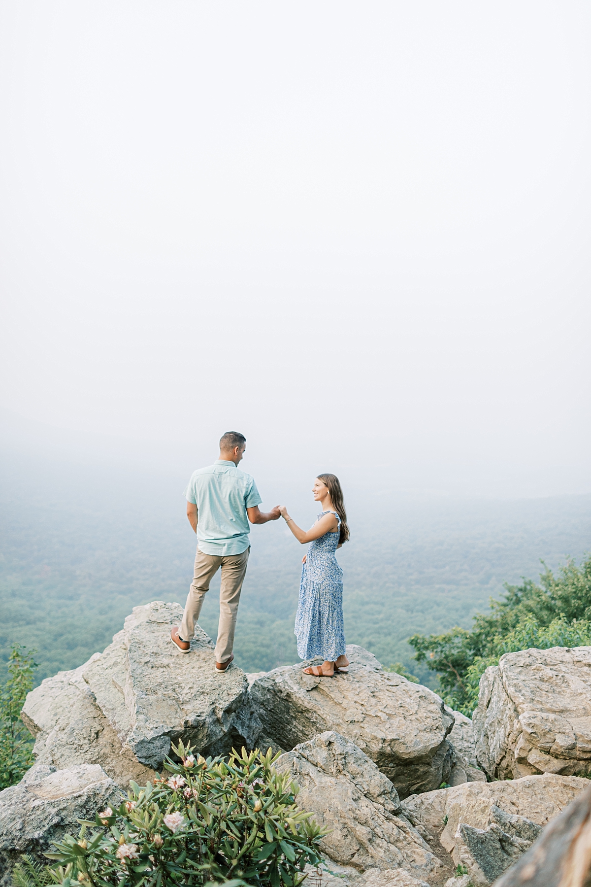 Engagement photo of a couple at Hawk Mountain Sanctuary in PA. The couple stands on rocks with a beautiful view